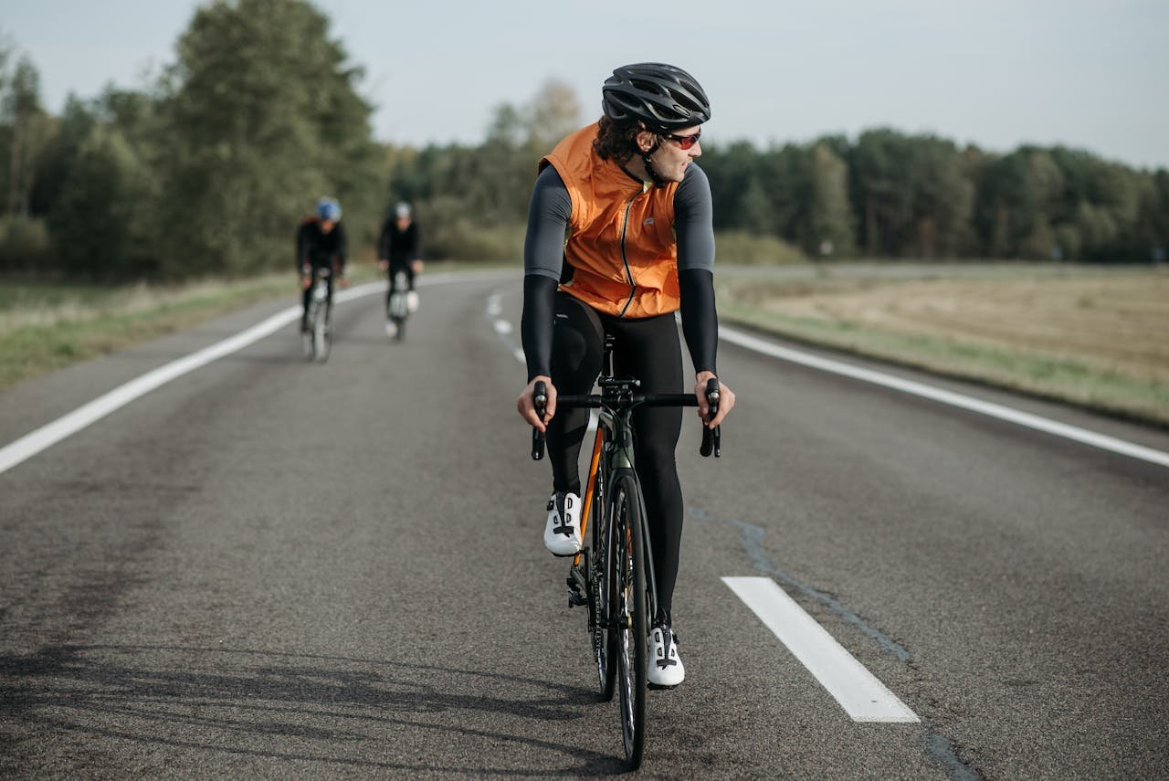 Cyclists in bright gear riding on a scenic countryside road during the day.